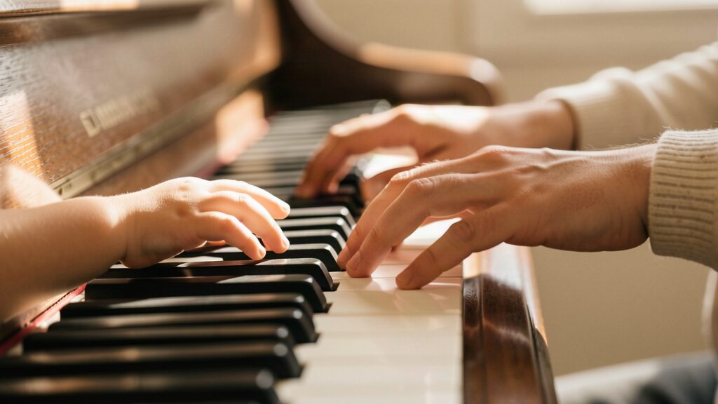 A child's hands and a teacher's hands on the piano keys
